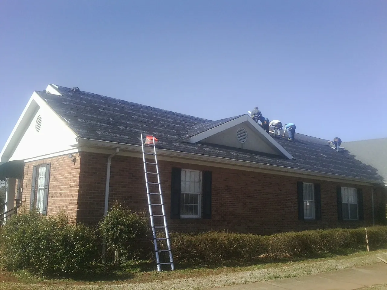 Crew tearing shingles off a brick ranch roof with a ladder set — Emergency Roof Repair work by our crew in Jerusalem